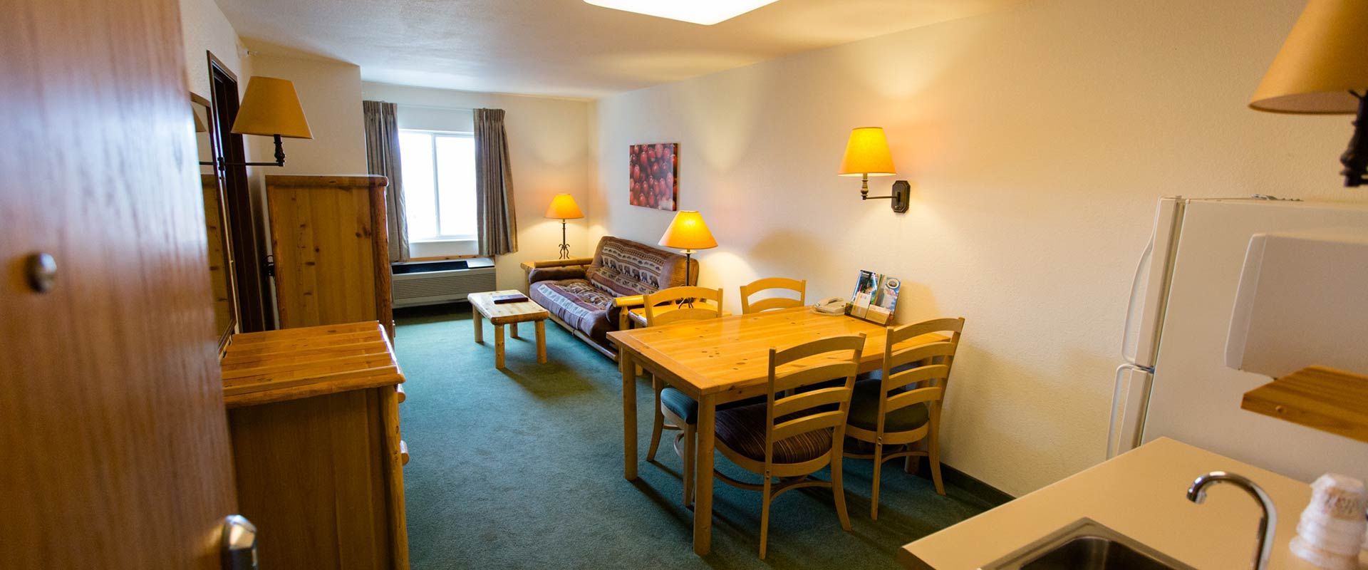 Hotel room interior with green carpet, a small table, sofa, and dining table.