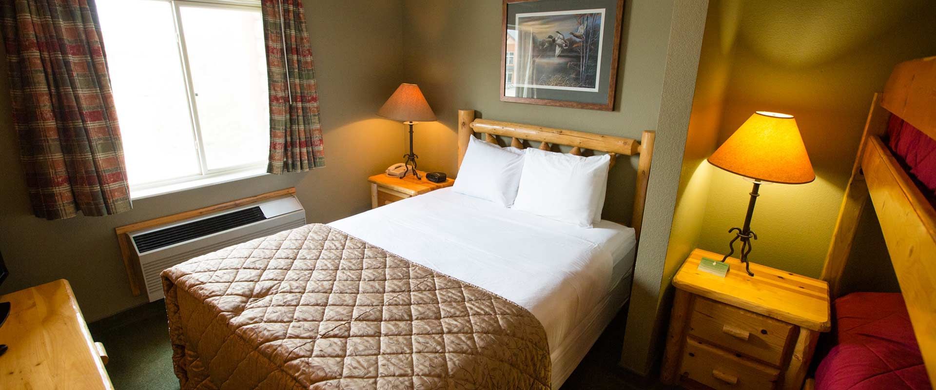 A hotel room with a bed, nightstands, and bunk beds. There's a window and a landscape painting.