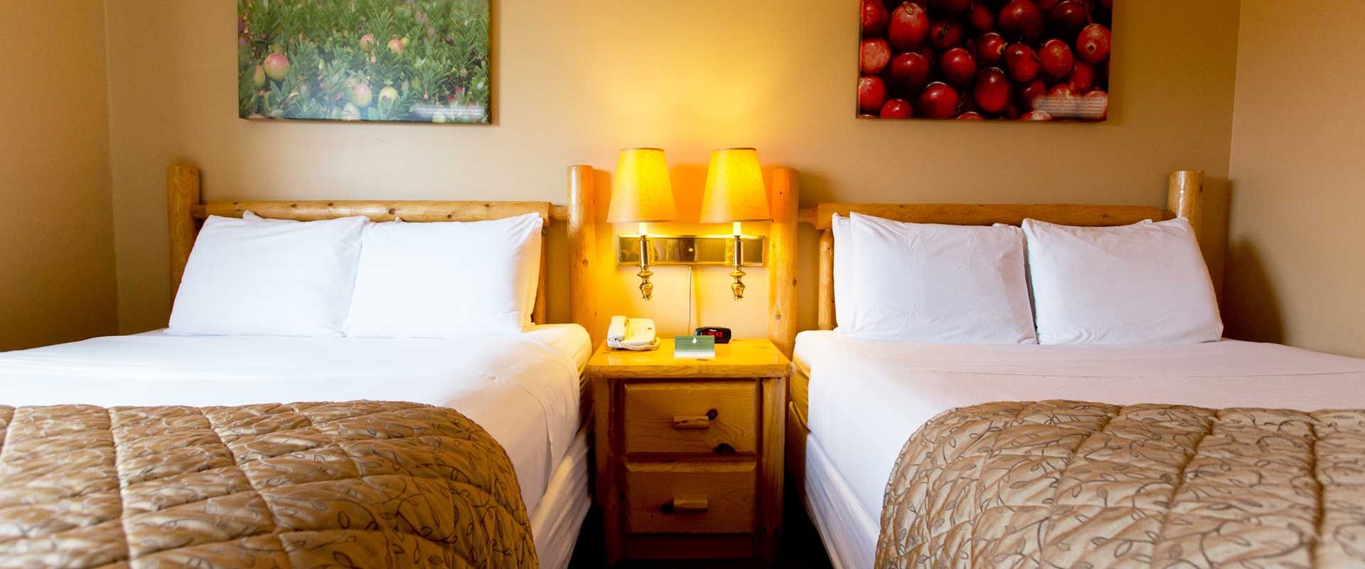 Two beds in a hotel room with white bedding, a nightstand, and wall art.