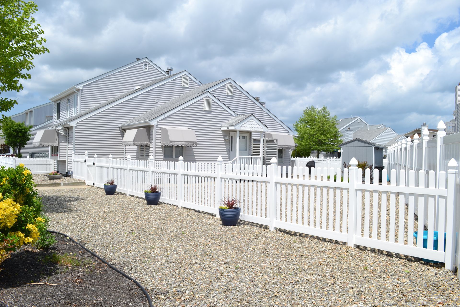 White house with white picket fence and gravel driveway under a cloudy sky