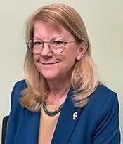 Smiling woman in glasses and blue blazer against a plain background