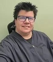 Person with short spiky hair and glasses smiling in a dark gray shirt against a light green background