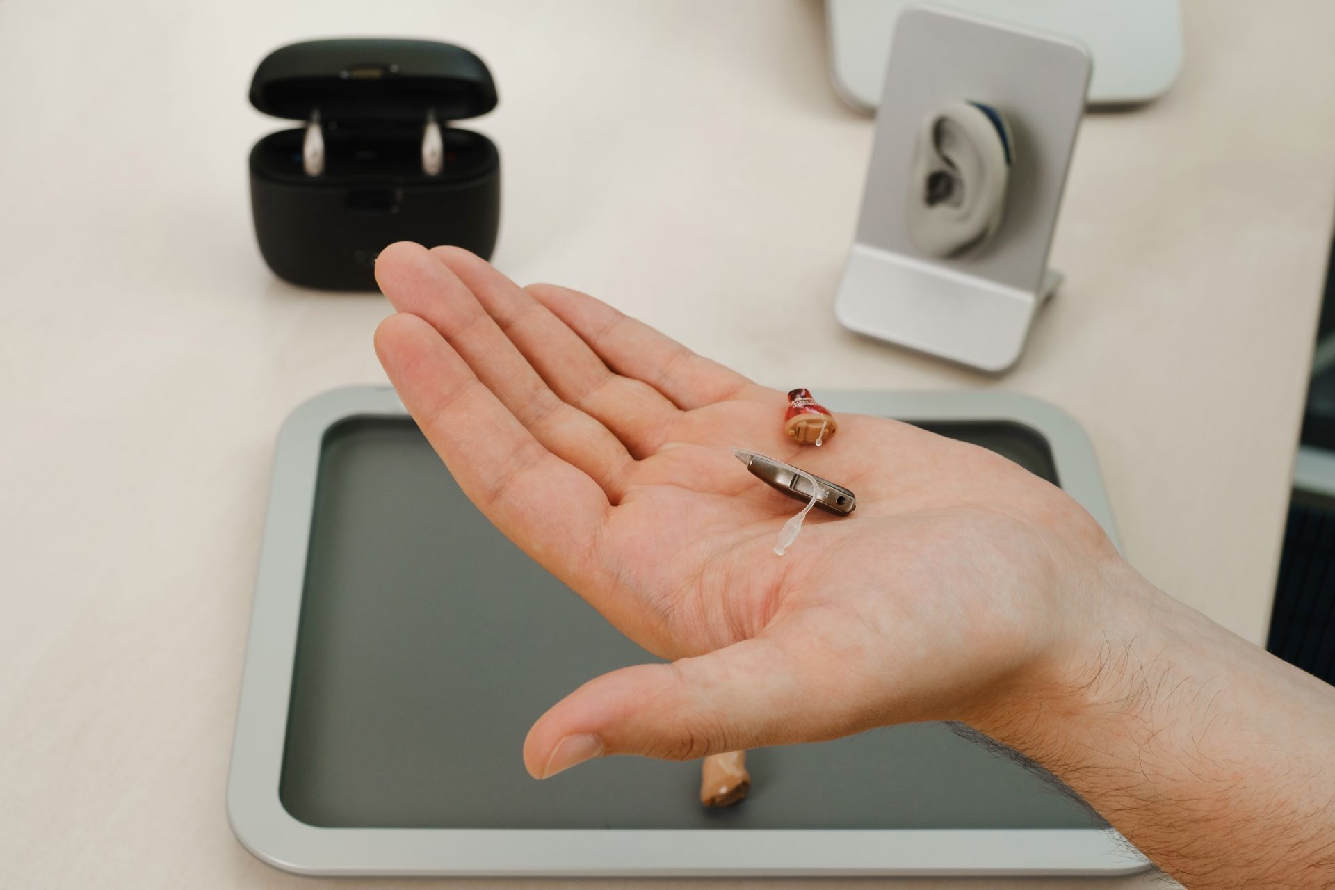 Open hand over a tray with small metal and wooden items on a desk