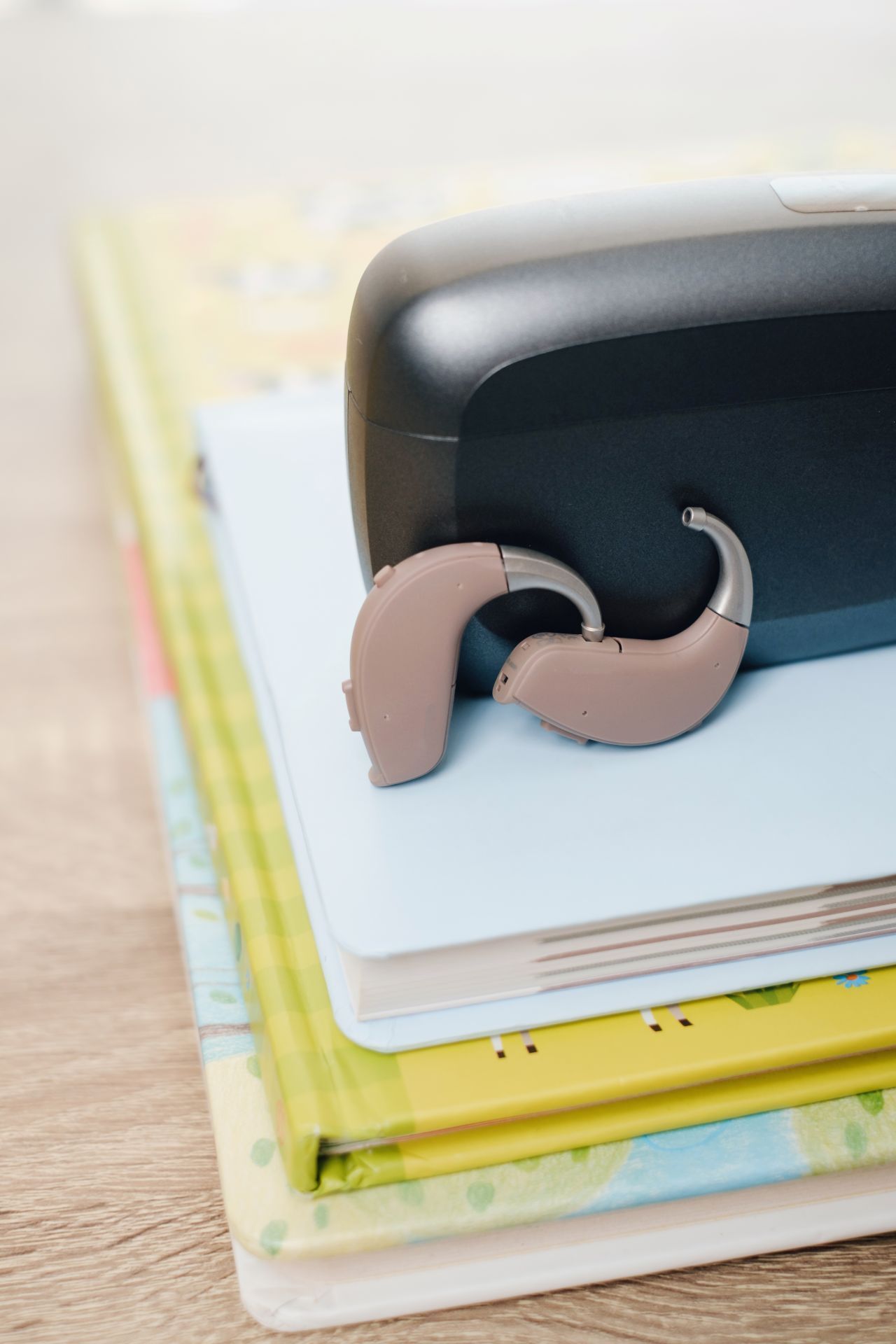 A hearing aid resting on a stack of colorful notebooks on a wooden table.