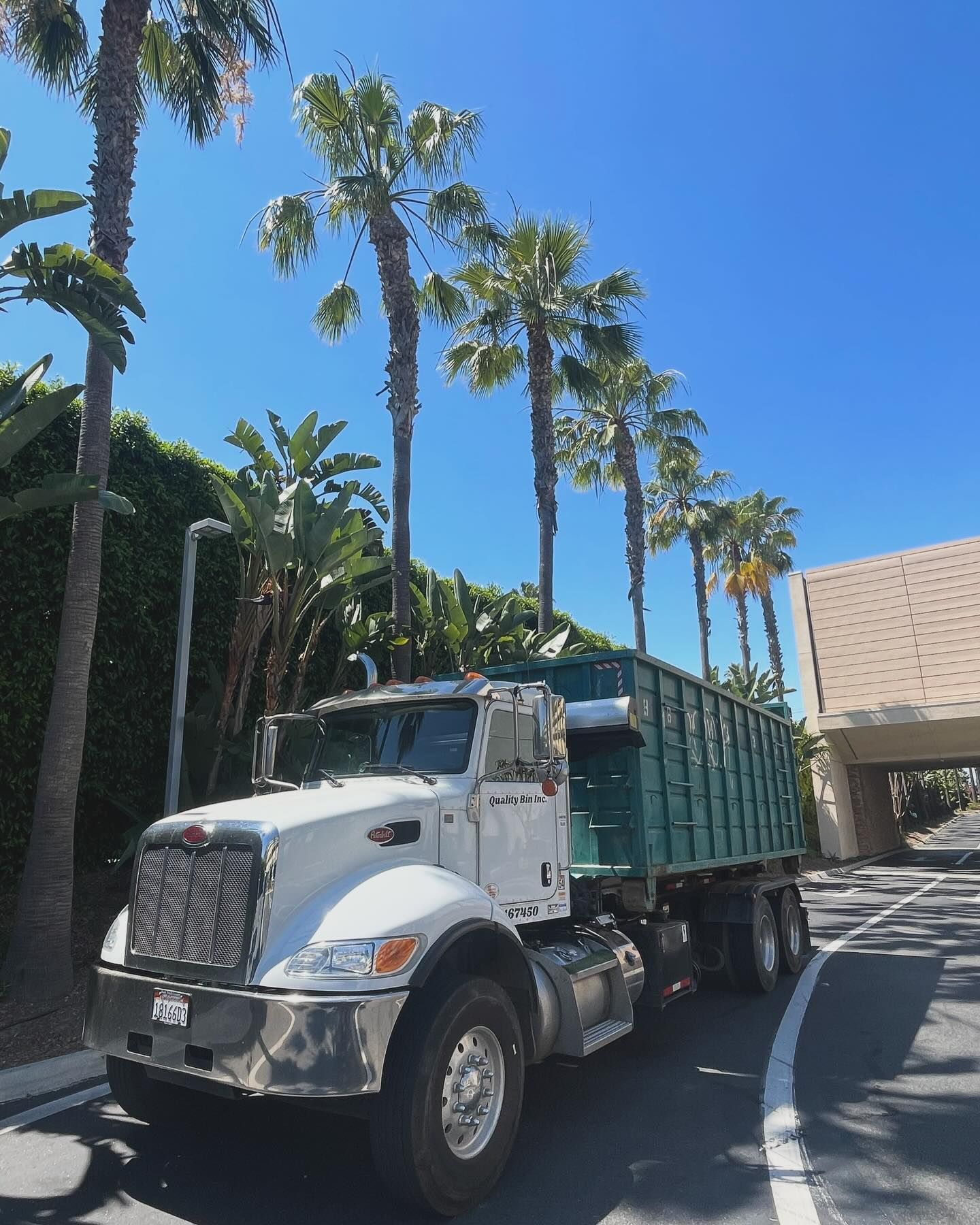 Quality Bin Inc. truck hauling a green roll-off dumpster Quality Bin Inc. truck hauling a green roll-off dumpster