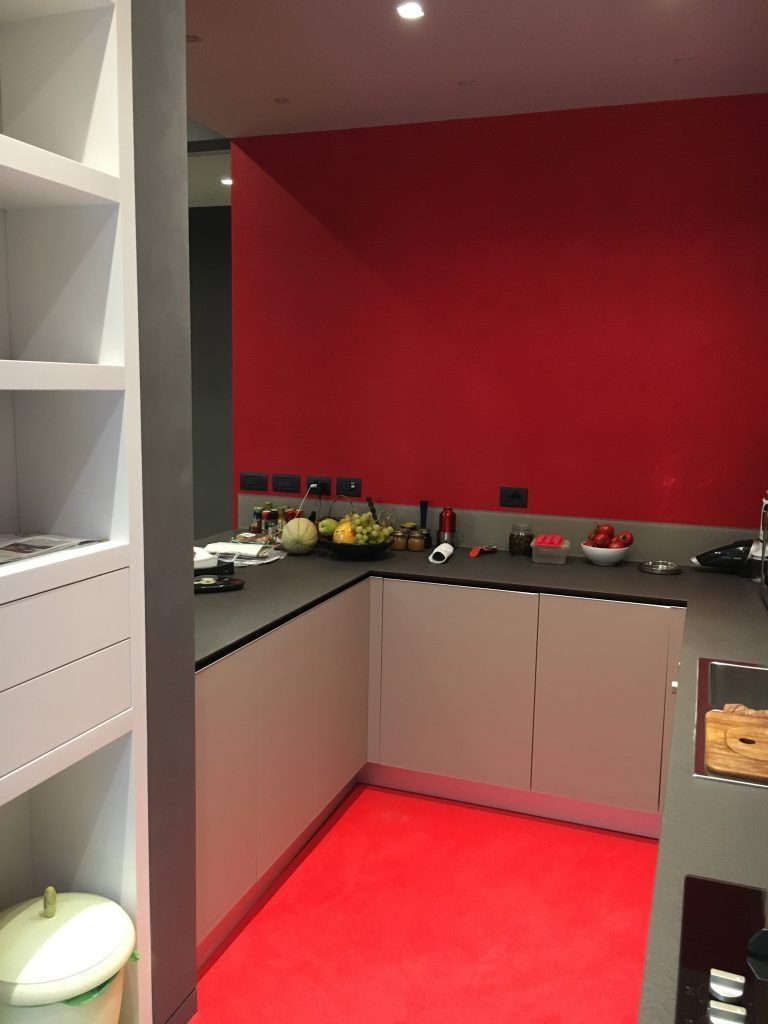 Cucina moderna con parete d'accento rossa, mobili grigi, piano di lavoro nero e tappeto rosso.