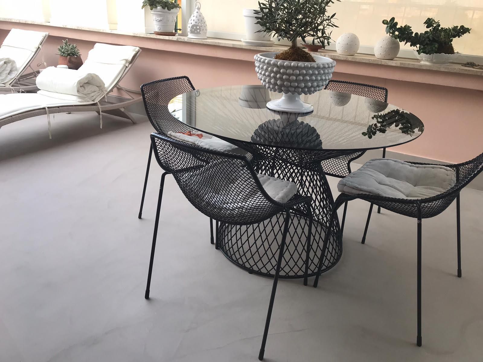 Zona salotto esterna con tavolo e sedie in filo metallico nero, accanto a una poltrona bianca e piante in vaso.