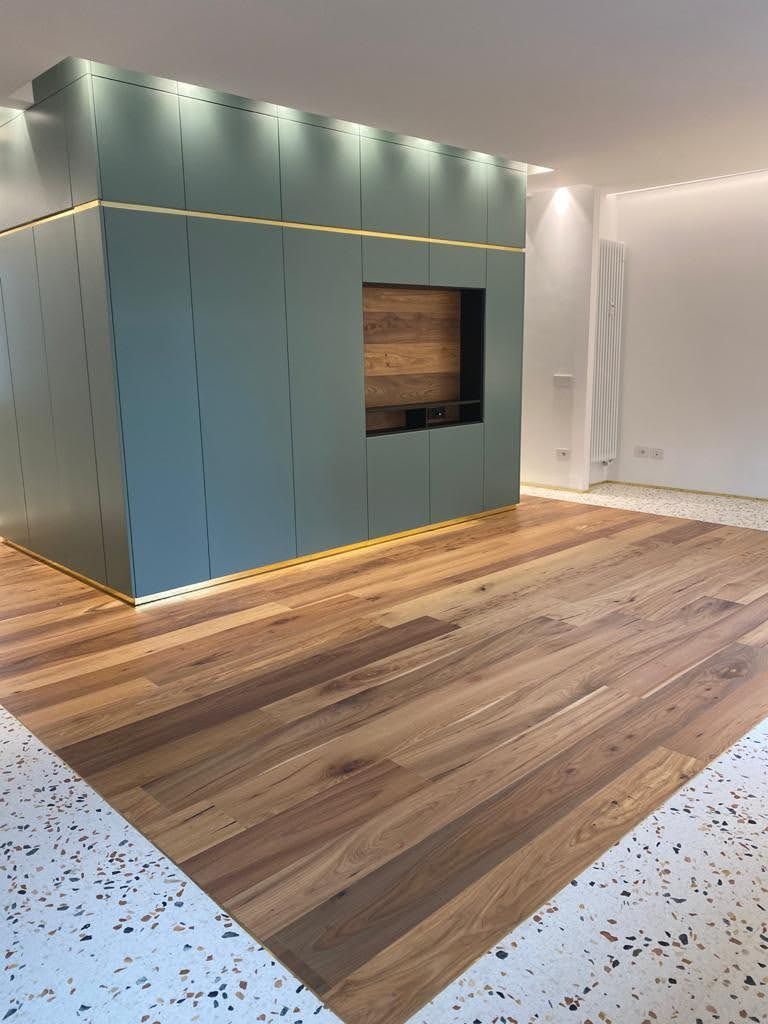 Stanza moderna e vuota con pavimento in legno, mobile a muro color verde acqua e faretti a incasso a soffitto.