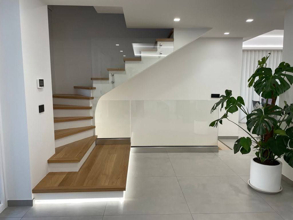 Scala interna moderna con gradini in legno, pareti bianche, pavimento piastrellato e una pianta in vaso.