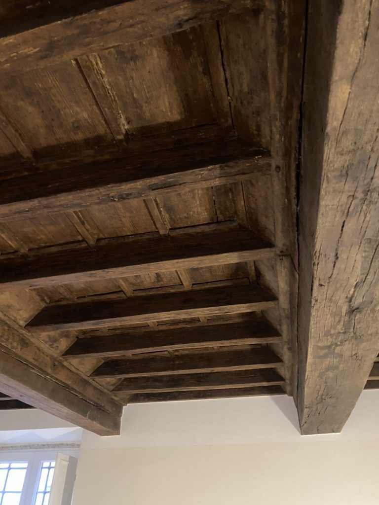 Travi e pannelli in legno sul soffitto di una stanza bianca con una finestra sottostante.