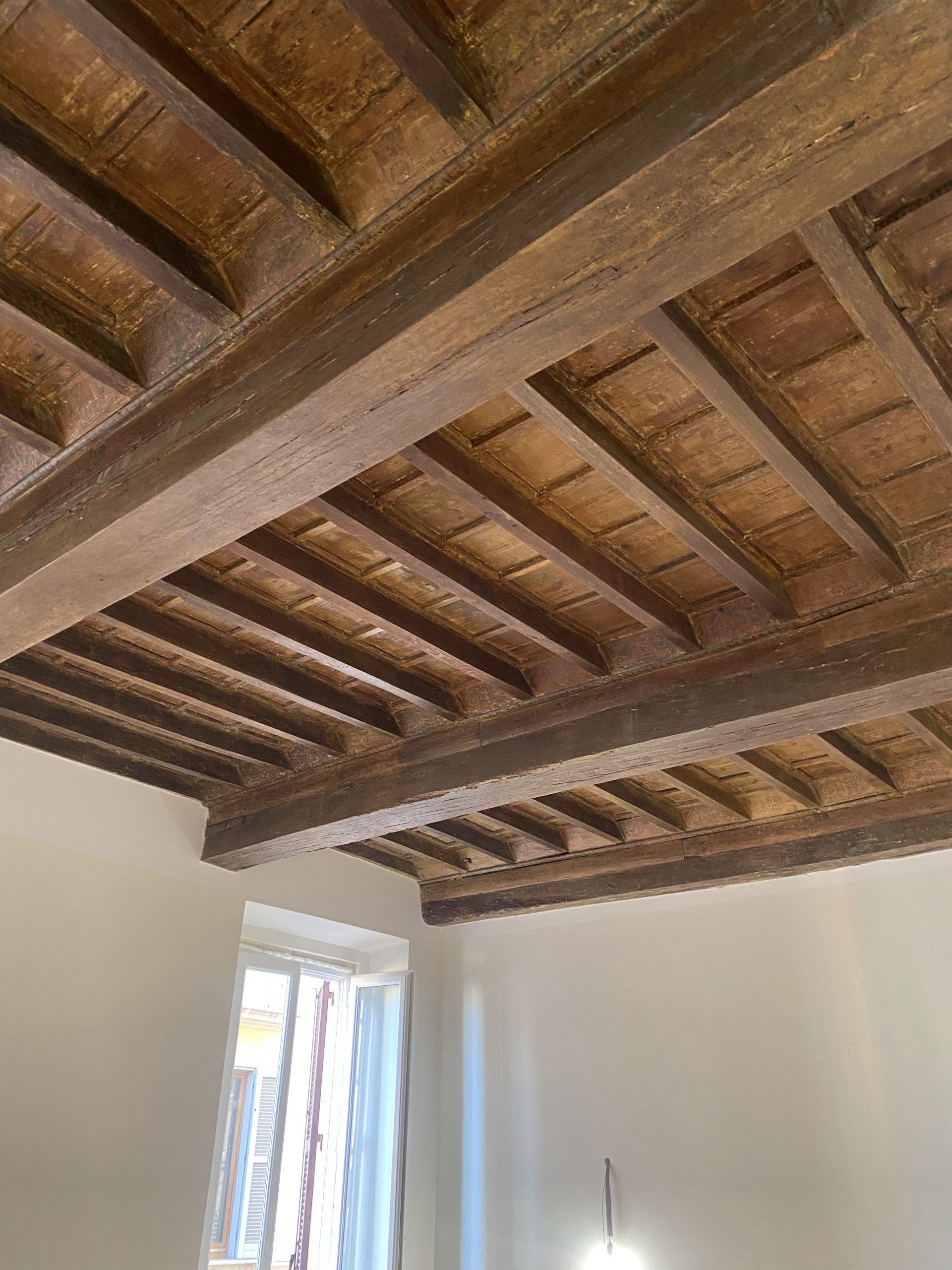 Soffitto con travi in legno e piastrelle in terracotta sopra una stanza bianca con finestra