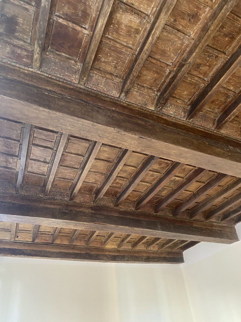 Soffitto con travi in legno scuro a vista sopra pareti bianche e semplici.