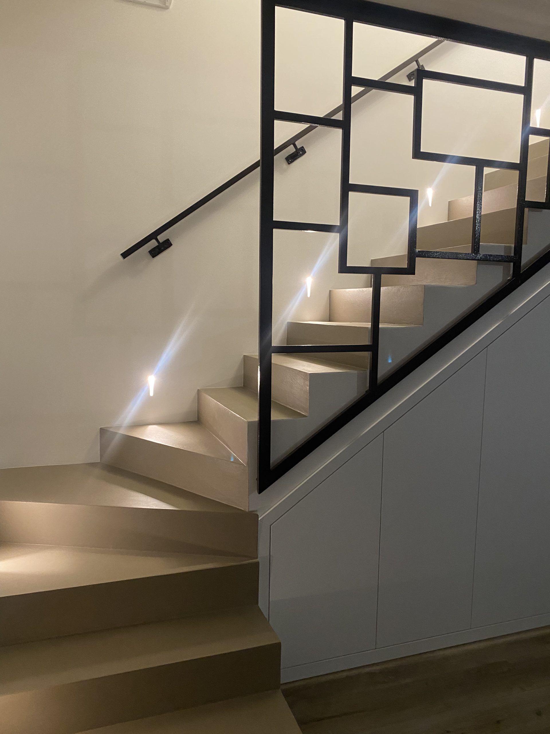 Scala interna curva con gradini rivestiti di moquette beige e ringhiera in metallo nero su una parete bianca.