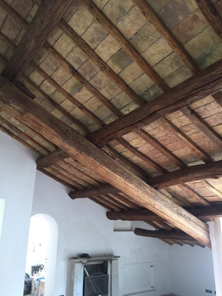 Stanza bianca con travi in legno a vista sul soffitto e tegole del tetto, vista dal basso.