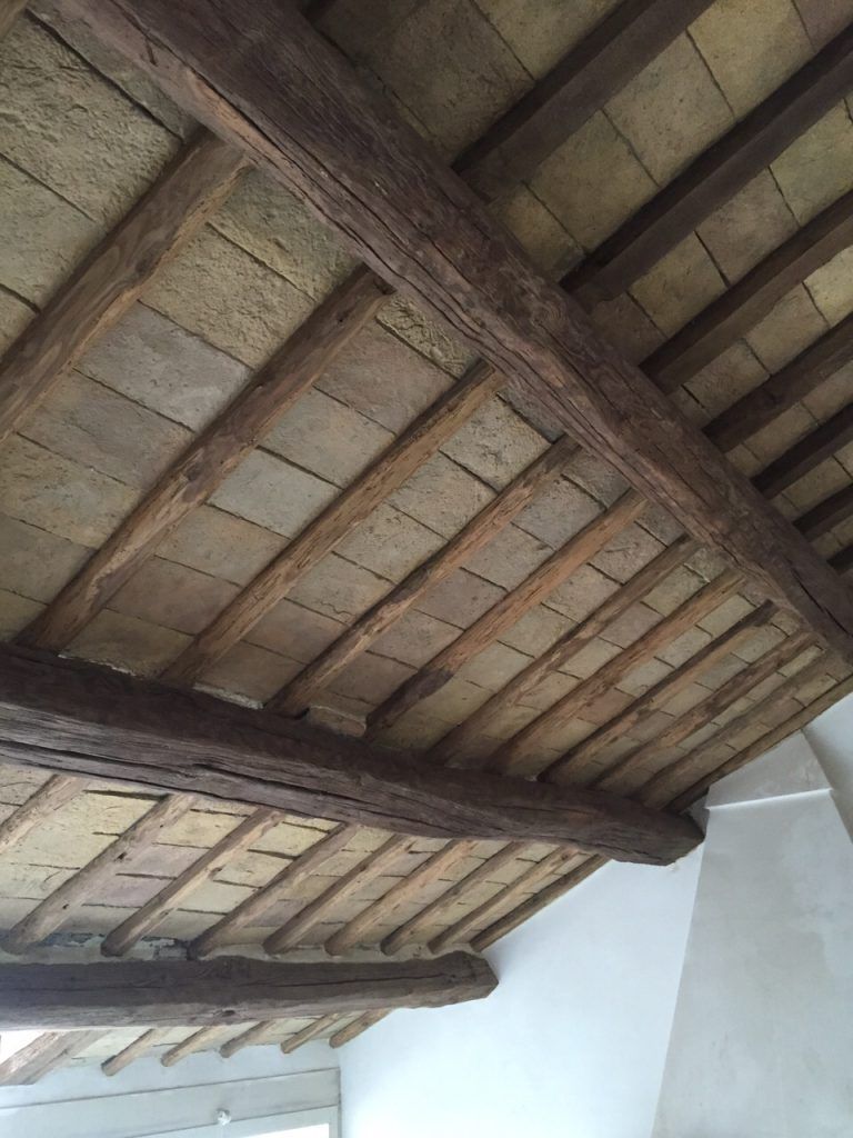 Soffitto con travi in legno antiche e travetti a vista sopra pareti bianche