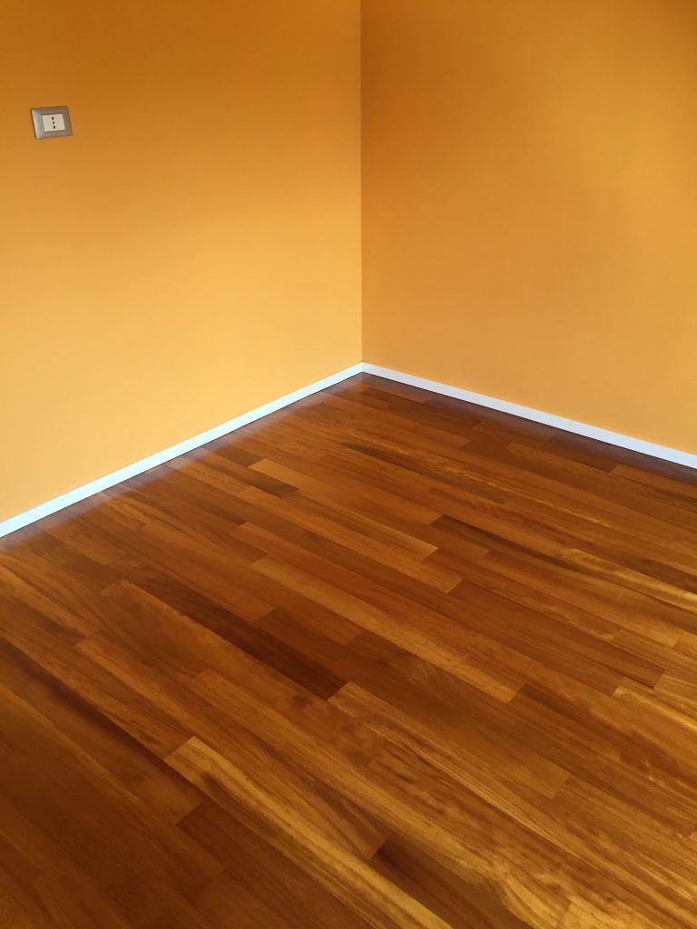 Angolo di una stanza vuota con pareti arancioni, finiture bianche e pavimento in legno.