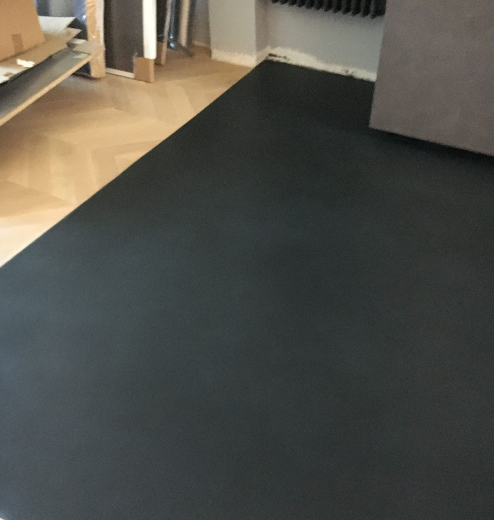 Tappeto nero su un pavimento in legno chiaro accanto a un divano grigio e a delle mensole in un soggiorno.