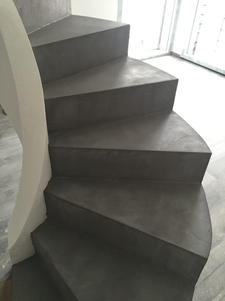 Scala curva rivestita di moquette scura con pareti bianche e luce naturale proveniente dalle finestre vicine.