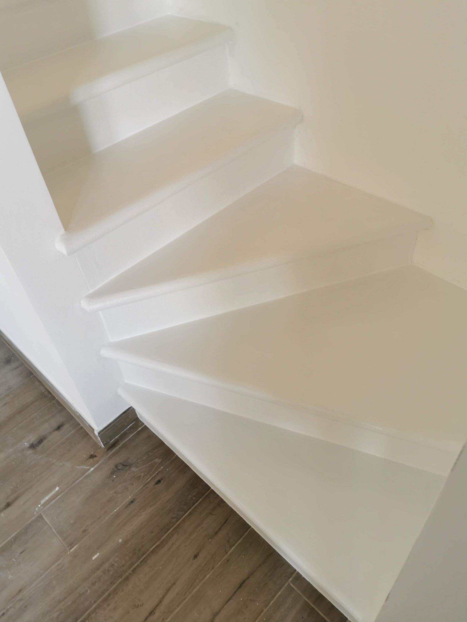 Scala bianca sospesa con gradini angolari accanto a un pavimento in legno chiaro in un interno minimalista