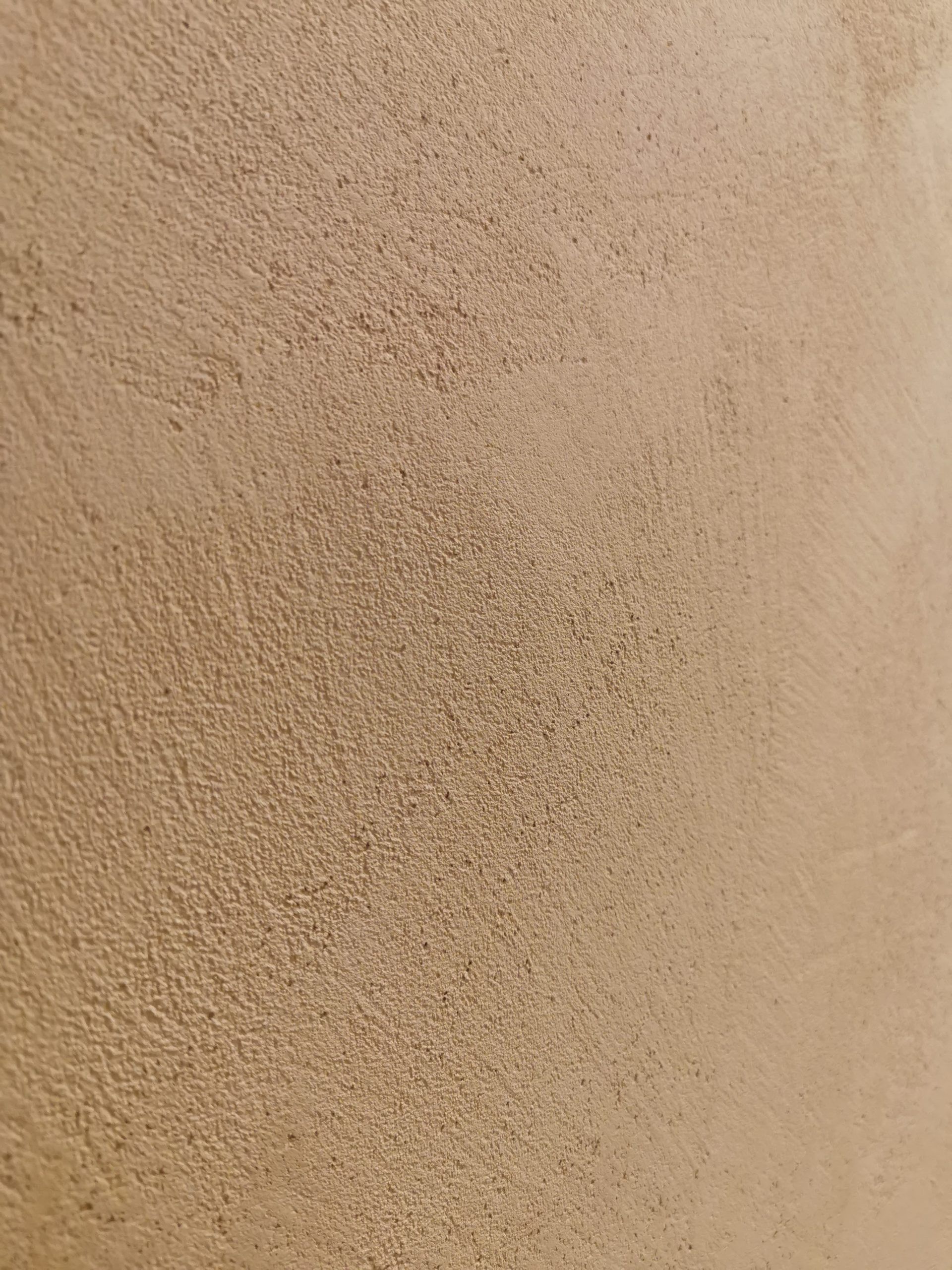 Primo piano di una superficie murale beige con texture e ombre delicate.