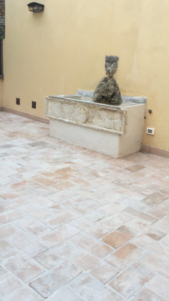 Scultura in pietra su una panchina bassa in un cortile beige con pavimento piastrellato.