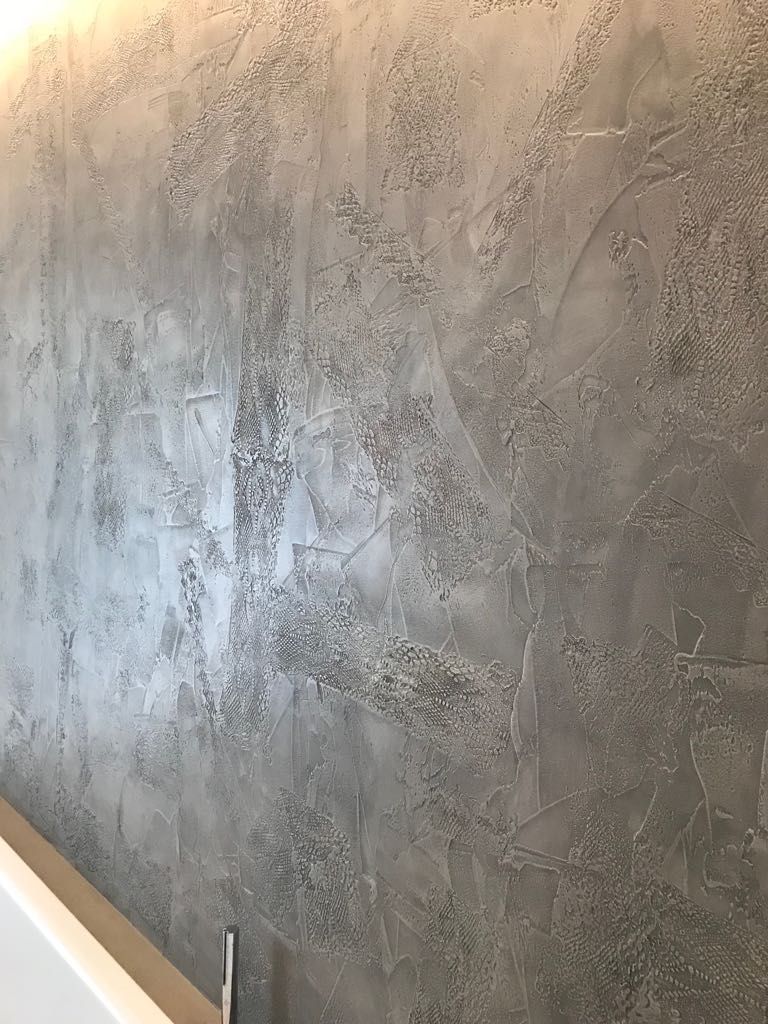 Parete intonacata di grigio con finitura ruvida e ringhiera bianca per le scale nell'angolo inferiore sinistro.