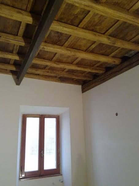 Soffitto rustico in legno sopra una stanza bianca con finestra e pareti color crema.