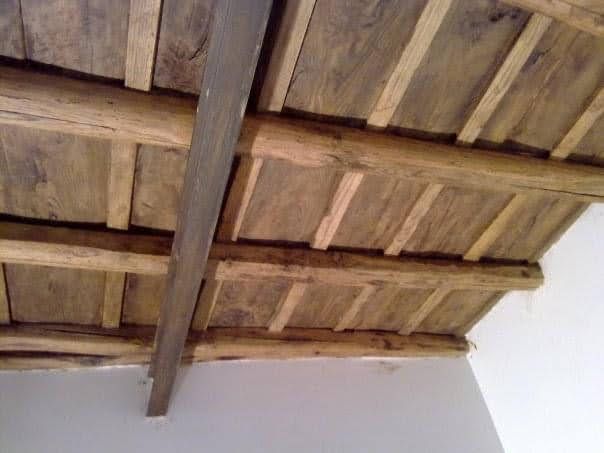 Soffitto in legno con travi a vista e assi consumate dal tempo sopra una parete bianca