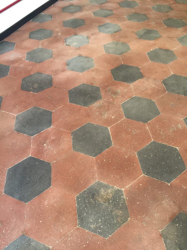 Piastrelle esagonali nere incastonate in un vialetto pavimentato di colore marrone rossastro.