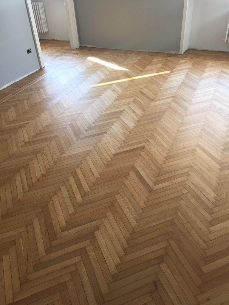 Stanza vuota con pavimento in legno chiaro a spina di pesce e luce del sole che filtra attraverso