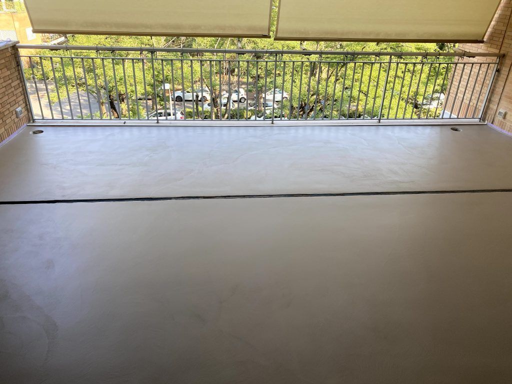 Patio coperto con pavimento piastrellato e ringhiera, affacciato su un giardino verde.