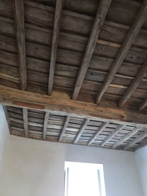 Travi in legno a vista sul soffitto, sopra una parete bianca e un'apertura finestrata all'interno di una stanza.