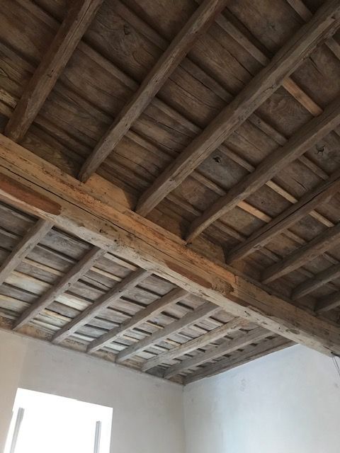 Soffitto con travi in legno a vista sopra pareti interne bianche e una luminosa apertura finestrata.