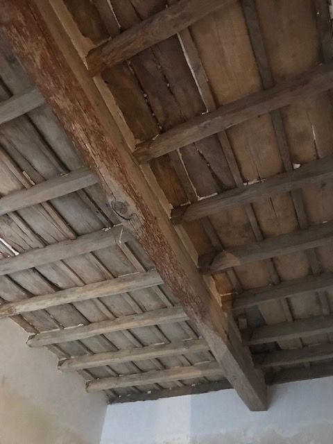 Primo piano di un soffitto in legno con travi a vista e travetti consumati dagli agenti atmosferici in una stanza