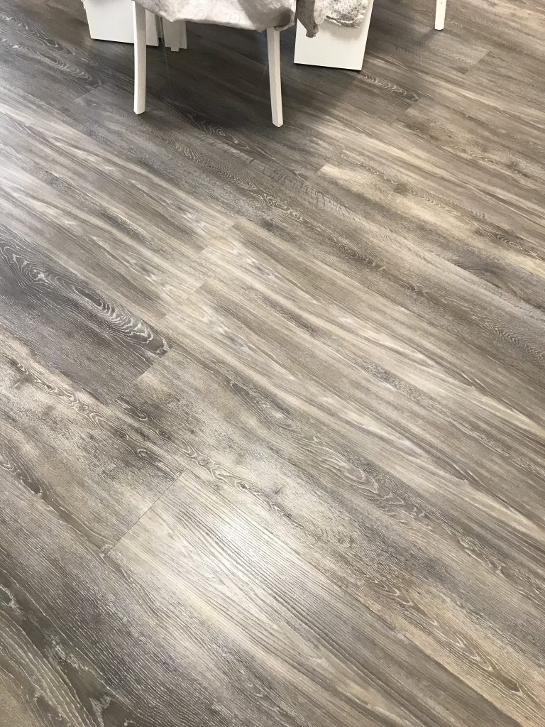 Pavimento grigio effetto legno con parte di sedia e tavolo visibili sul bordo superiore.