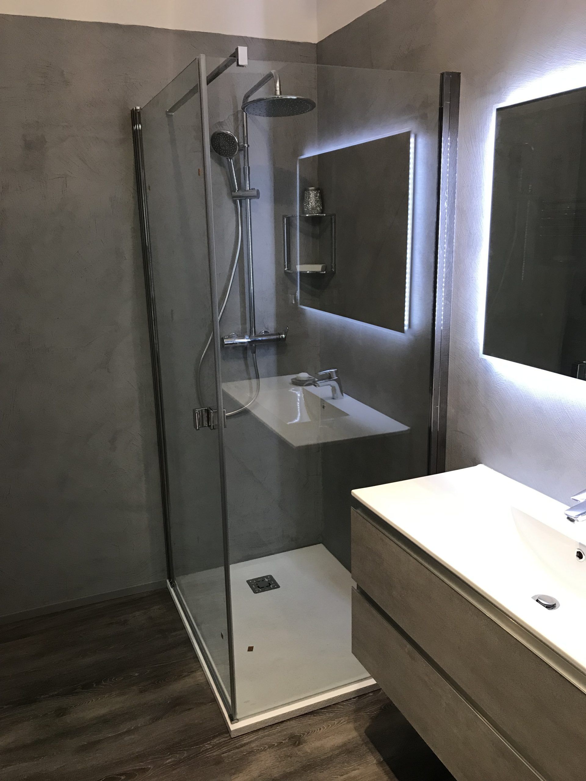 Bagno moderno con doccia in vetro, lavabo con mobiletto e specchio illuminato.