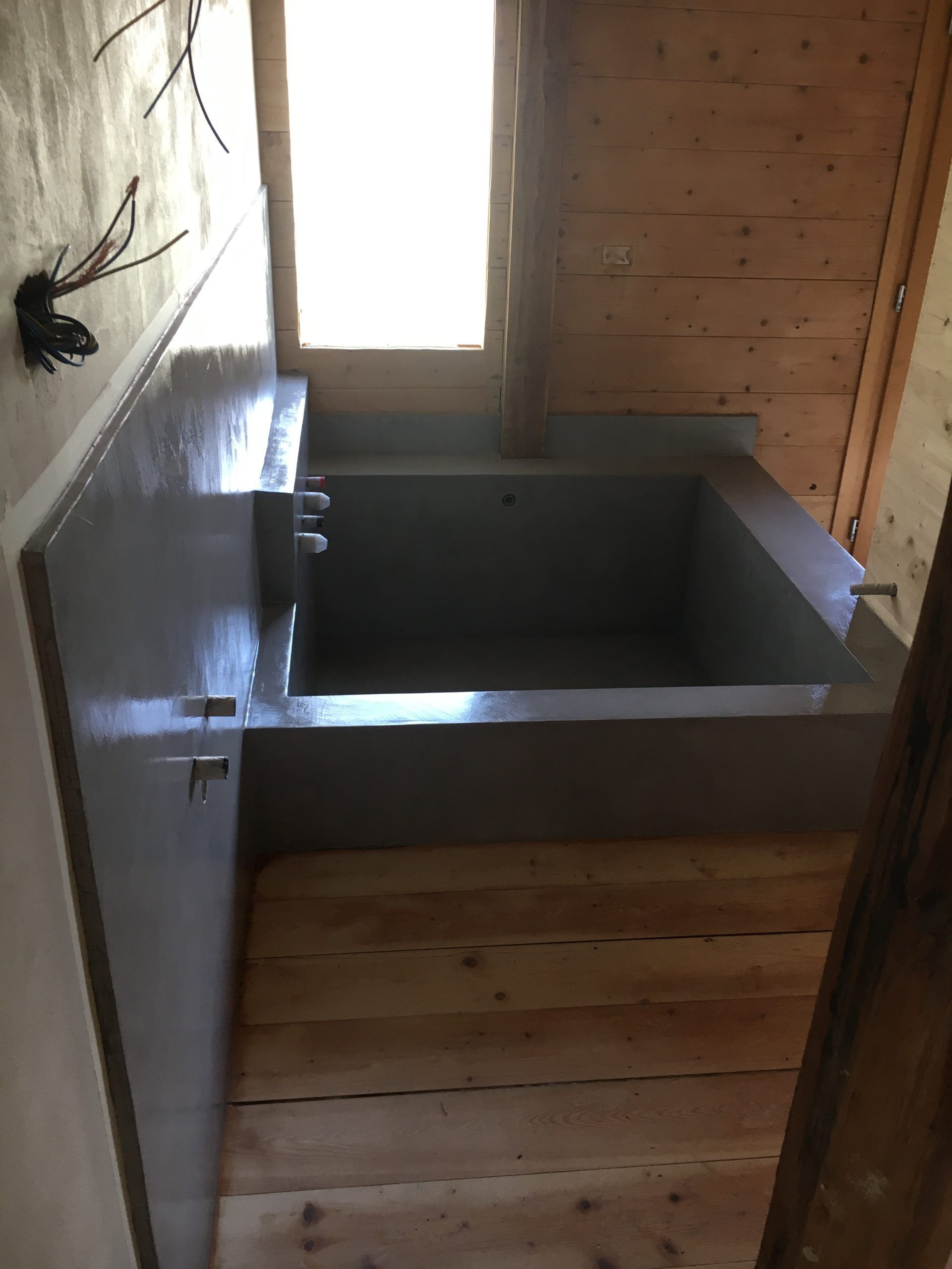 Piccolo bagno in legno con vasca grigia sotto una finestra e soffitto inclinato.
