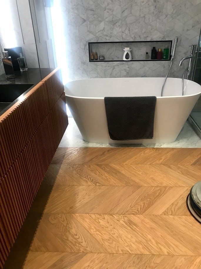 Bagno moderno con vasca freestanding bianca, asciugamano scuro, pavimento in legno e nicchia con mensola sopra la vasca.