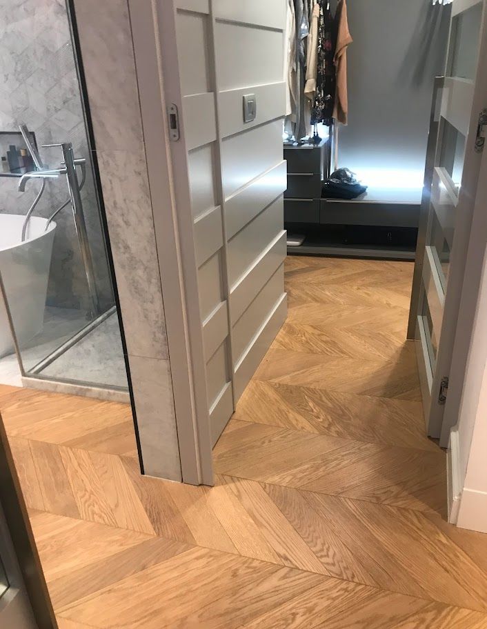 Corridoio con pavimento in legno a spina di pesce, porte grigie, armadio con specchio e cabina armadio oltre