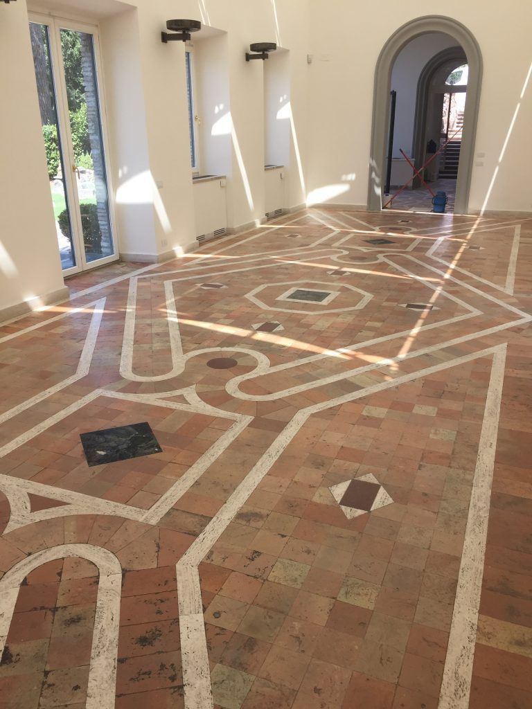 Corridoio soleggiato con piastrelle in terracotta e motivi geometrici bianchi che conduce a una porta ad arco.