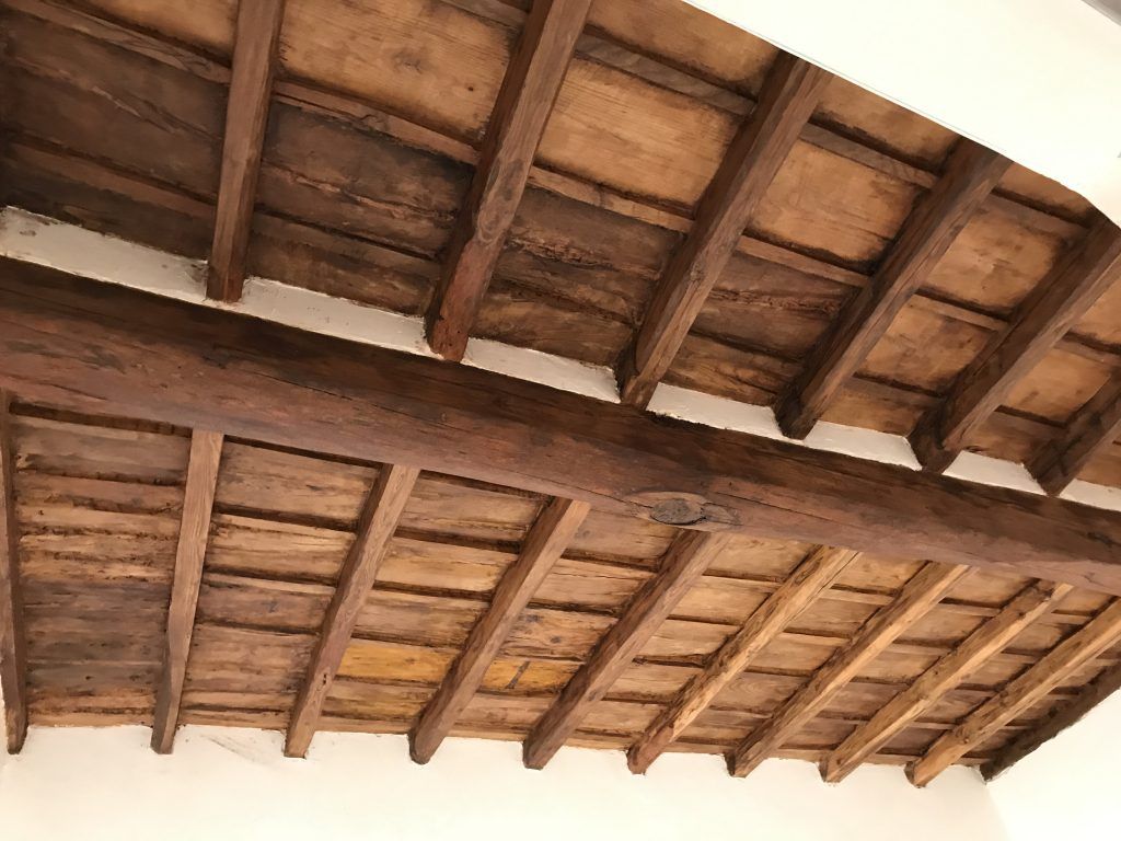 Soffitto in legno con travi a vista e tegole in terracotta, visto dal basso.