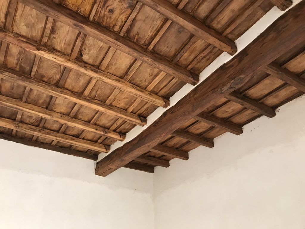 Travi in legno a vista e piastrelle in terracotta sopra pareti bianche in una stanza rustica
