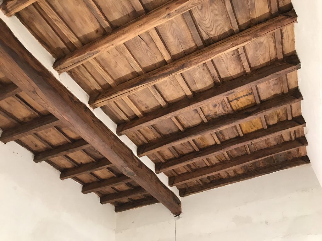 Travi in legno a vista e tegole in terracotta sopra pareti bianche in un interno rustico