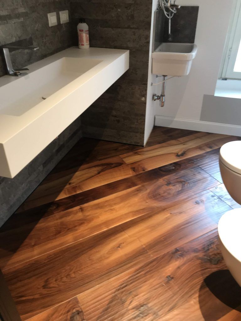 Bagno moderno con lavabo bianco, parete piastrellata in grigio e pavimento effetto legno vicino a una porta doccia in vetro.