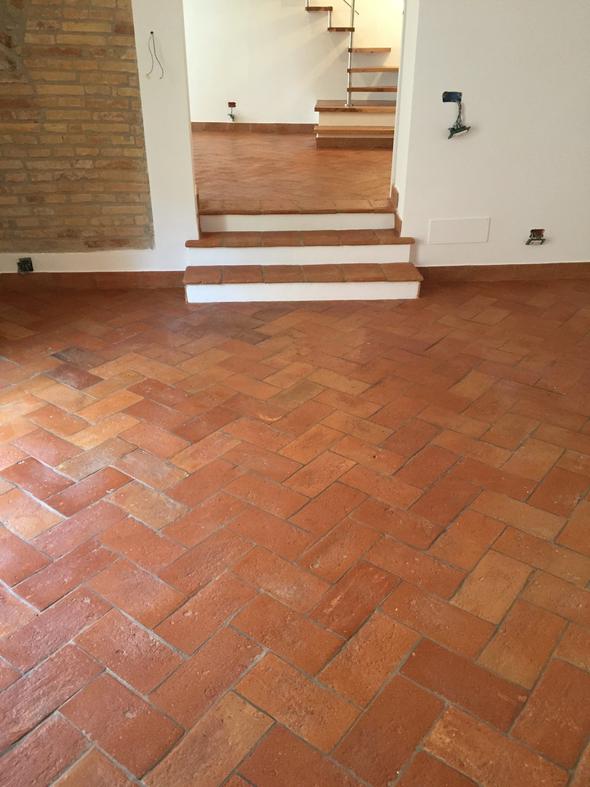 Stanza vuota con pavimento in mattoni a spina di pesce e una piccola scala che conduce a una porta.