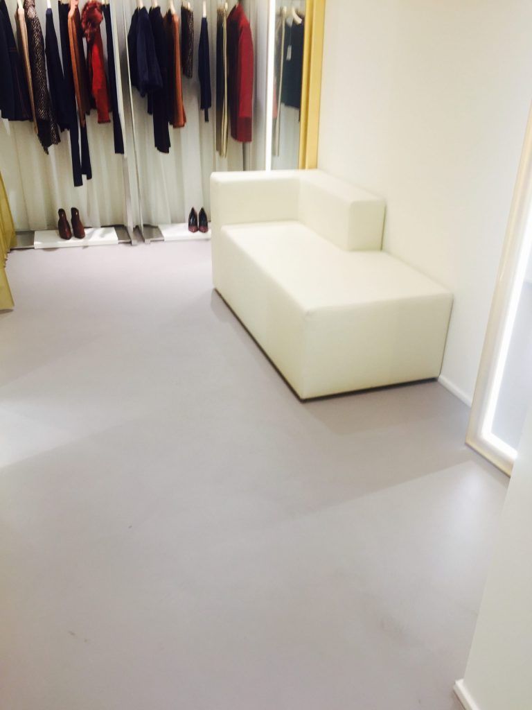Spogliatoio minimalista con abiti appesi e una panca componibile bianca su un pavimento grigio.