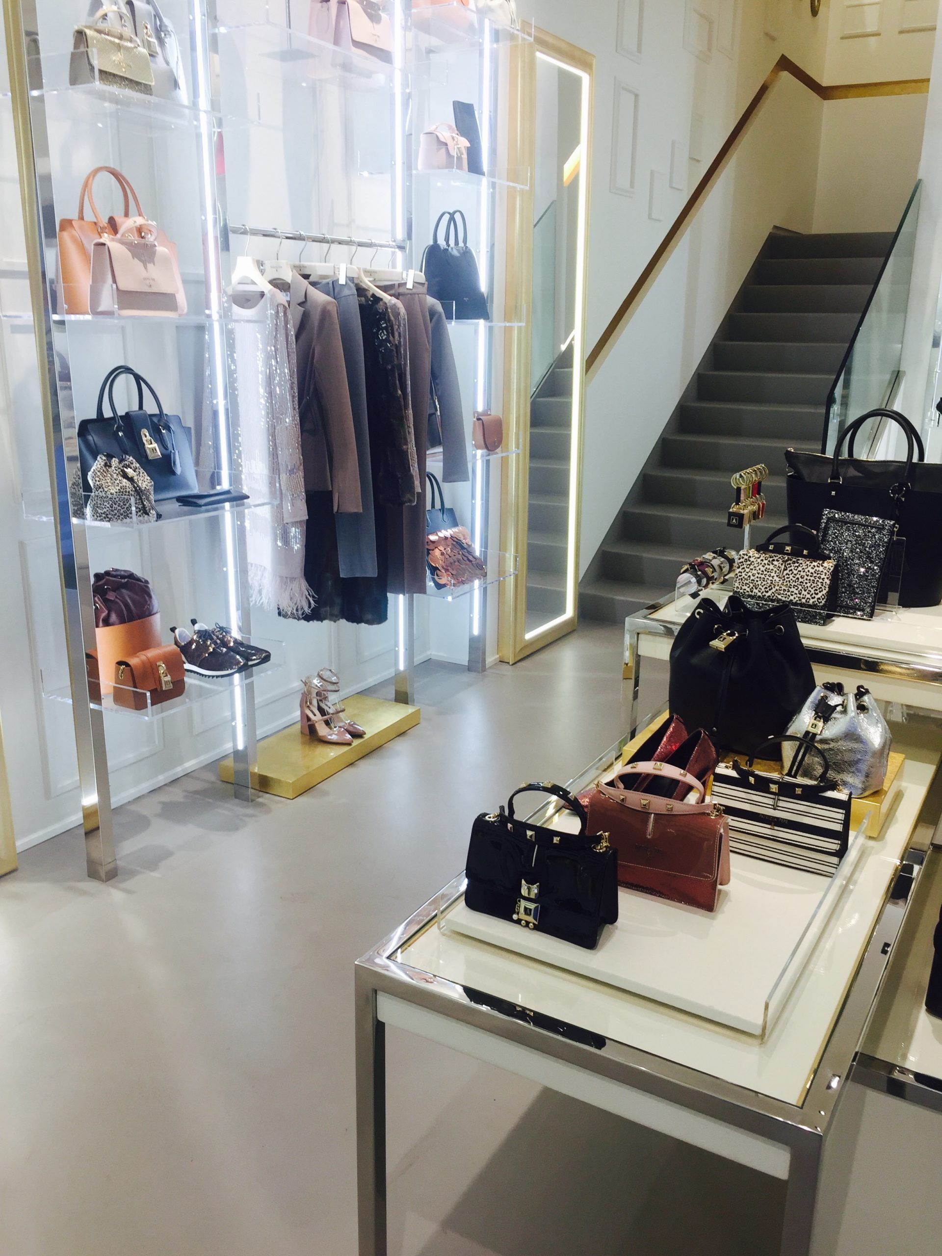 Esposizione in boutique con borse, appendiabiti e scale in un luminoso interno di negozio.