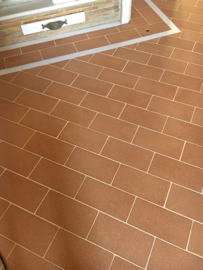 Pavimento in piastrelle color beige con fughe bianche accanto a una finestra con cornici bianche e modanature a parete.