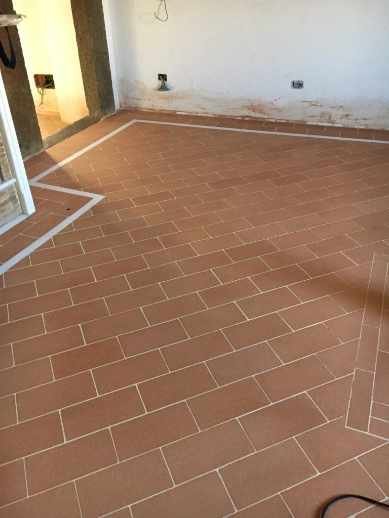 Stanza vuota con pavimento in piastrelle di terracotta, pareti bianche e porta aperta.