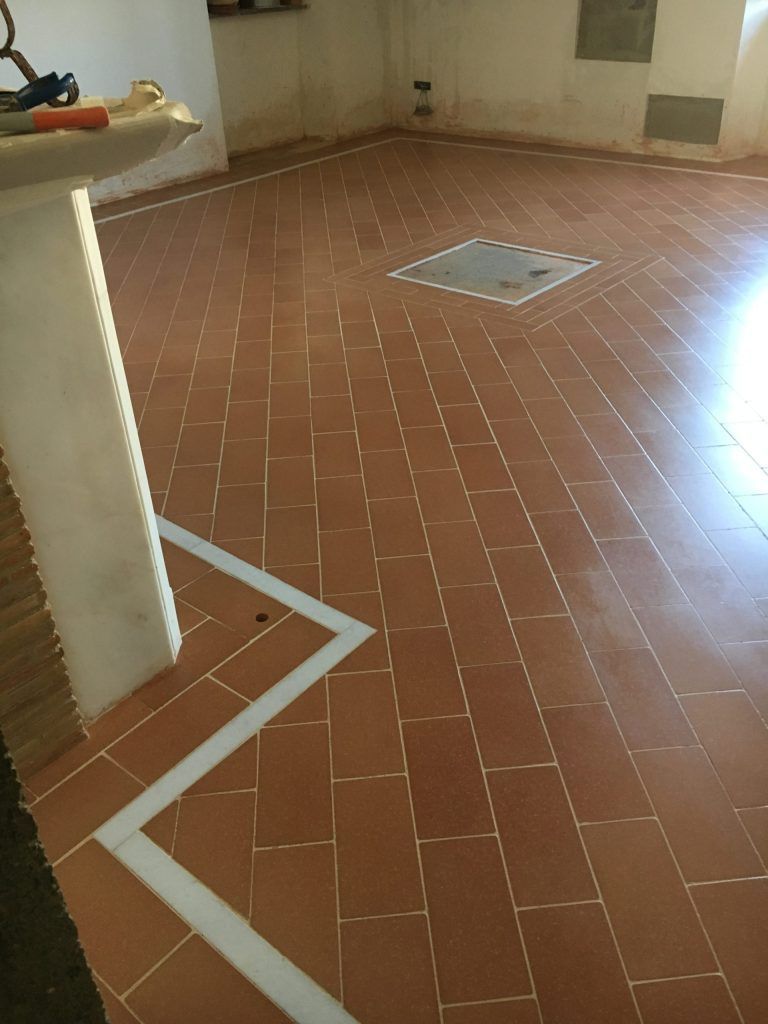 Stanza vuota piastrellata con pavimento in cotto, linee di confine bianche e uno scarico a pavimento vicino al centro.